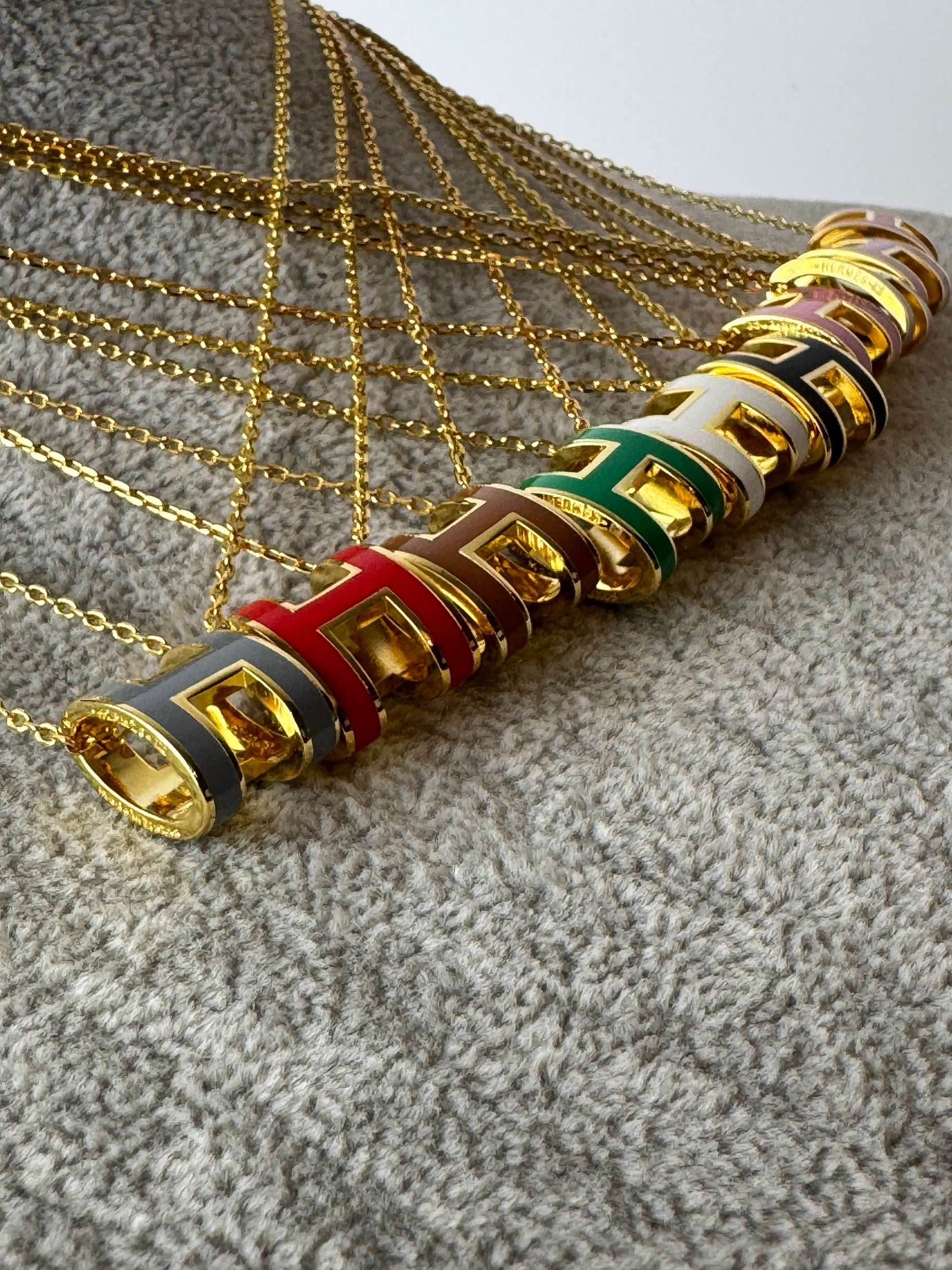 Yellow gold enamel H pendant necklaces arranged in rows by color