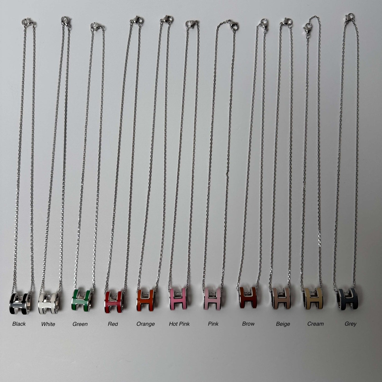 White gold enamel H pendant necklaces arranged in rows by color